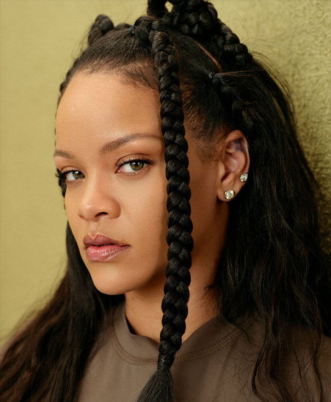 image of rihanna fresh faced against khaki colored background with thick braids in her hair