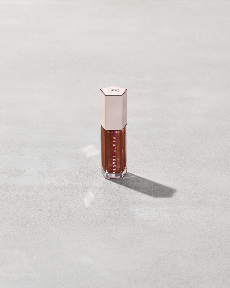 A close tube of Gloss Bomb Universal Lip Luminizer in the shade Hot Chocolit Fantasy on a grey background.
