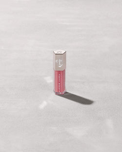 A closed tube of Gloss Bomb Universal Lip Luminizer in the shade Candy Soda on a grey background. A closed tube of Gloss Bomb Universal Lip Luminizer in the shade Candy Soda on a grey background.