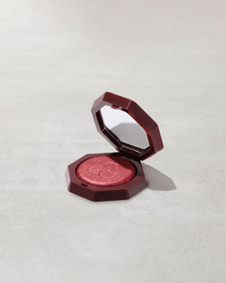 Open product shot of Hot Cheeks Velour Blushlighter in shade Cherry Pop on a concrete background. Open product shot of Hot Cheeks Velour Blushlighter in shade Cherry Pop on a concrete background.