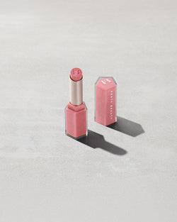 Open product shot of Gloss Bomb Stix Shimmer in shade Fussy on a concrete background. Open product shot of Gloss Bomb Stix Shimmer in shade Fussy on a concrete background.