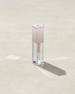 A closed tube of Gloss Bomb Universal Lip Luminizer in the shade Glass Slipper on a grey background. A closed tube of Gloss Bomb Universal Lip Luminizer in the shade Glass Slipper on a grey background.