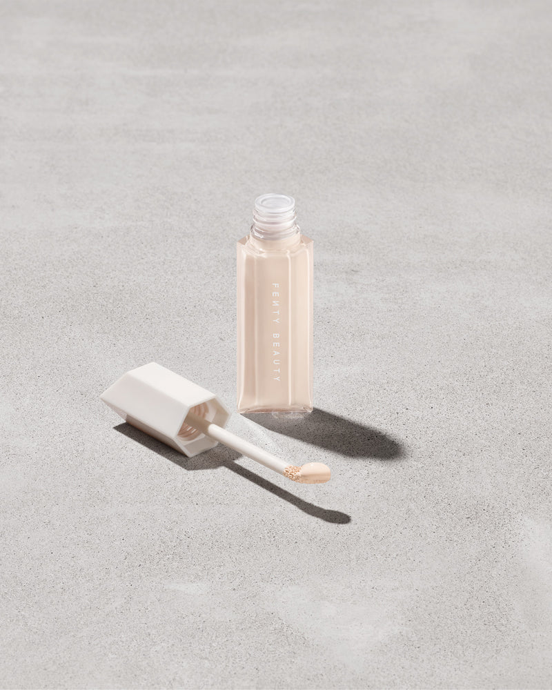 Open bottle of Fenty Beauty We're Even Hydrating Longwear Concealer with doe foot applicator in shade 100c on a concrete background.