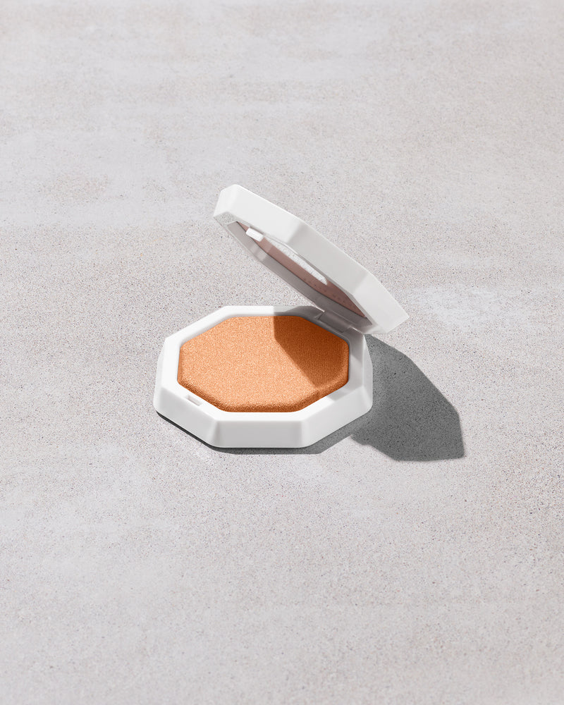 Open product shot of Demi'glow Light-Diffusing Highlighter in shade Yum Rum on a concrete backdrop.