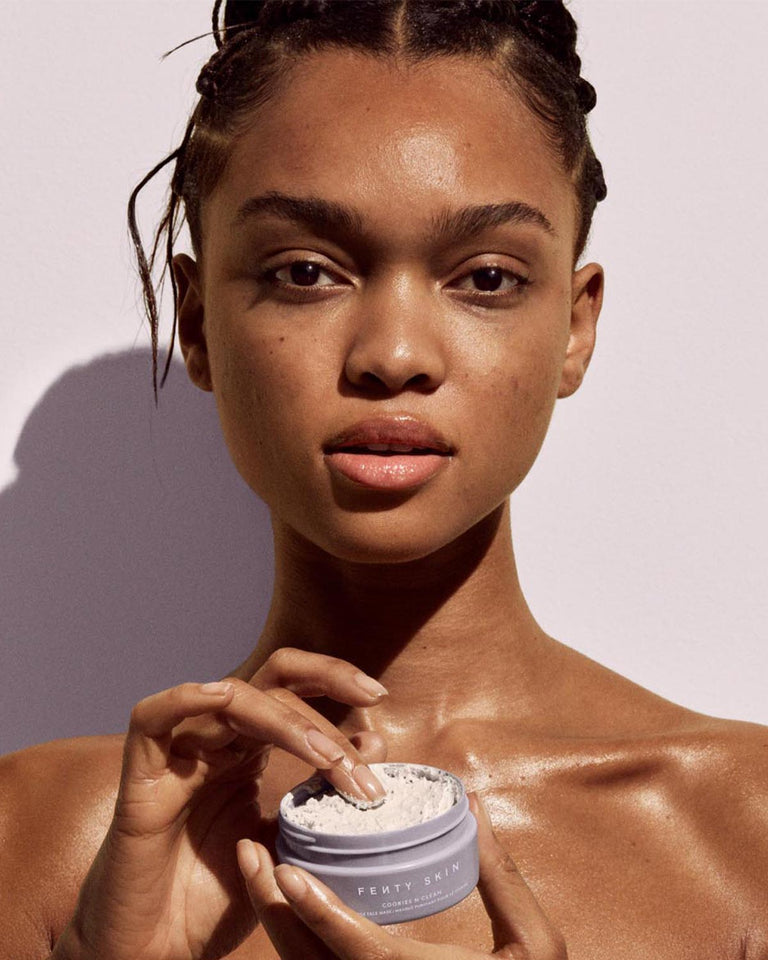 Model holding a container of Fenty Skin Cookies N Clean Whipped Clay Pore Detox Face Mask With Salicylic Acid + Charcoal.