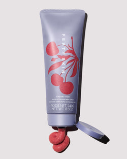 An open Cherry Dub Body Scrub bottle with product squirting out of it on a grey background.