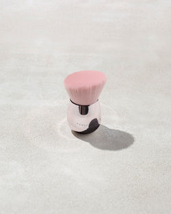 A fenty face and body kabuki brush with pink bristles on a gray background A fenty face and body kabuki brush with pink bristles on a gray background