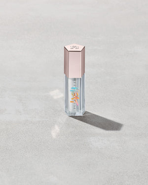 Closed tube of Gloss Bomb Heat lip gloss and plumper in the shade Glass Slipper on a grey background.