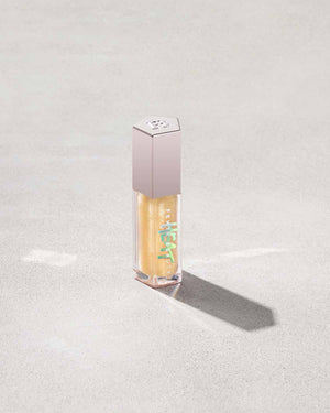 Closed tube of Gloss Bomb Heat lip gloss and plumper in the shade Lemon Lava on a grey background.