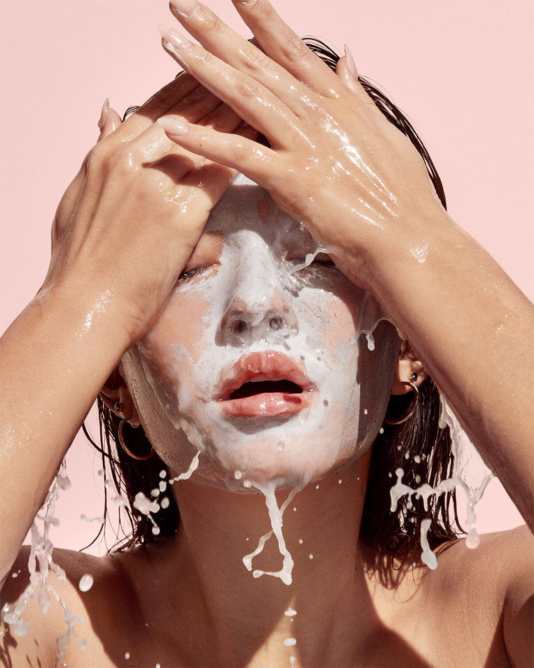 Model washing Cookies N Clean face mask off with water splashing on a pink background.