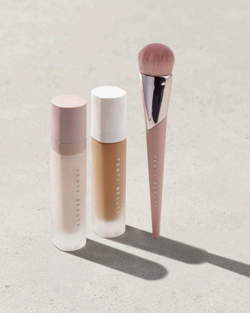 Fenty Beauty Primer, Pro Filter Soft Matte Foundation, and Foundation Brush 145 on a concrete background.