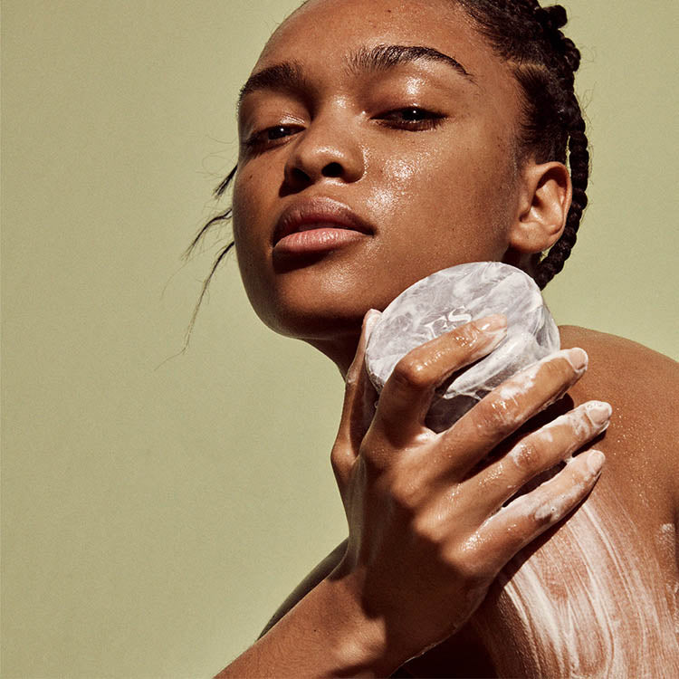medium skin toned model cleansing skin with brown round soap