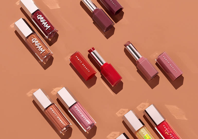 Fenty Beauty lip gloss collection on a peach background.