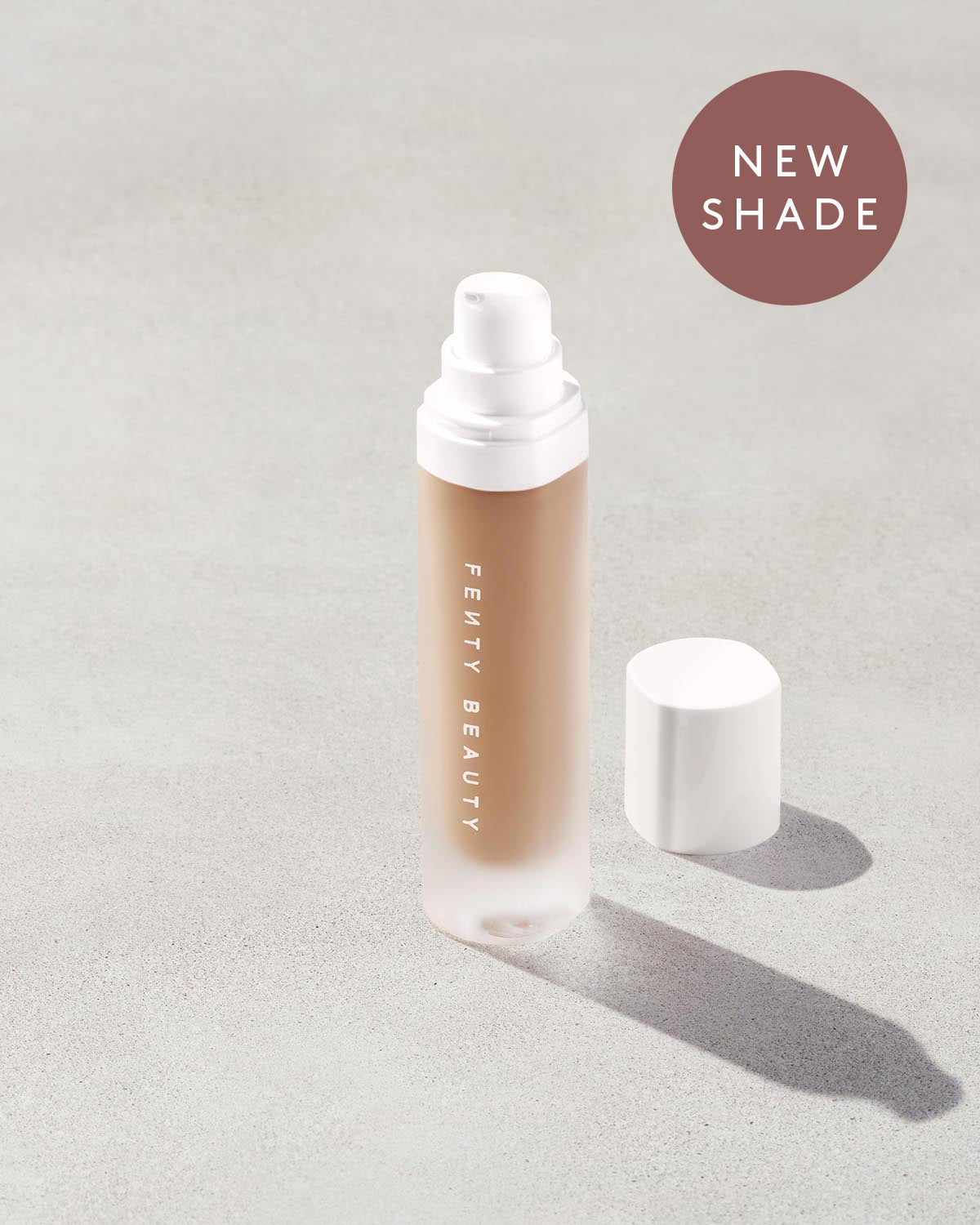 Open bottle of a new shade of Fenty Beauty Pro Filt'r Soft Matte Longwear Foundation with pump dispenser in shade #295 on concrete background