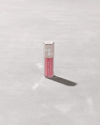 A closed tube of Gloss Bomb Universal Lip Luminizer in the shade Candy Soda on a grey background.