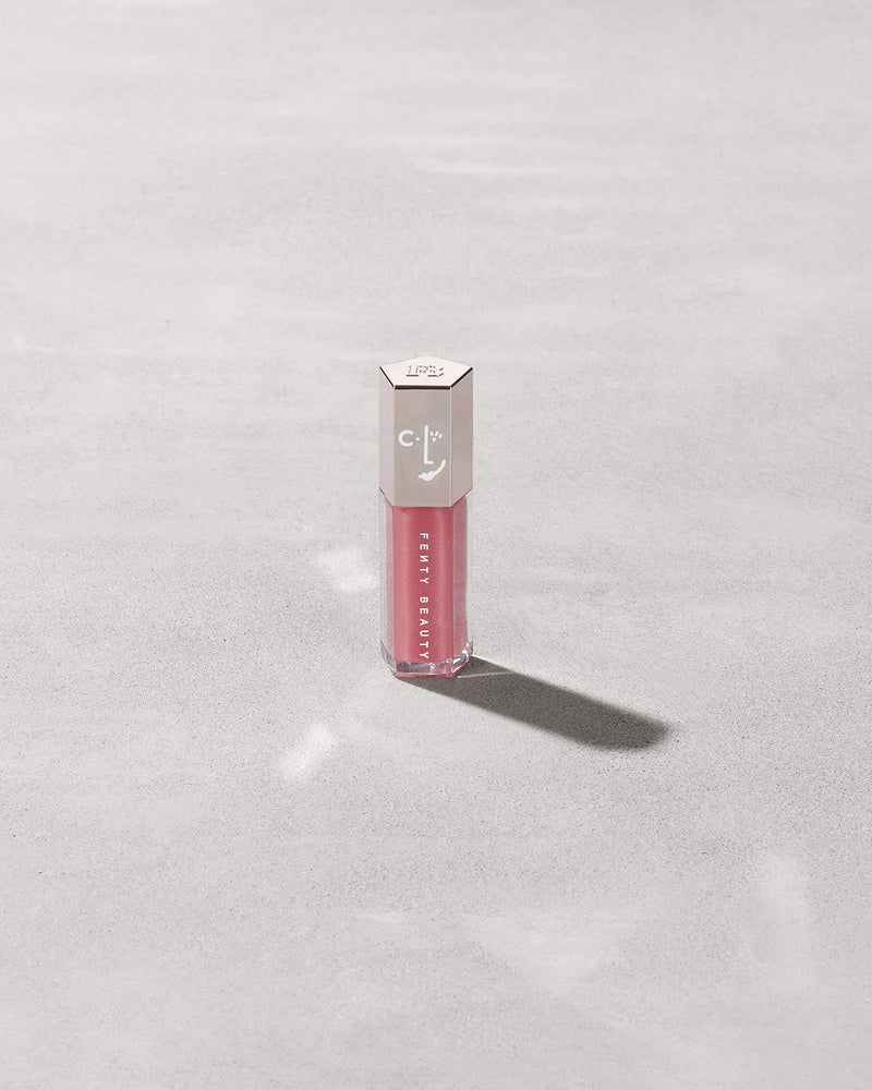 A closed tube of Gloss Bomb Universal Lip Luminizer in the shade Candy Soda on a grey background.