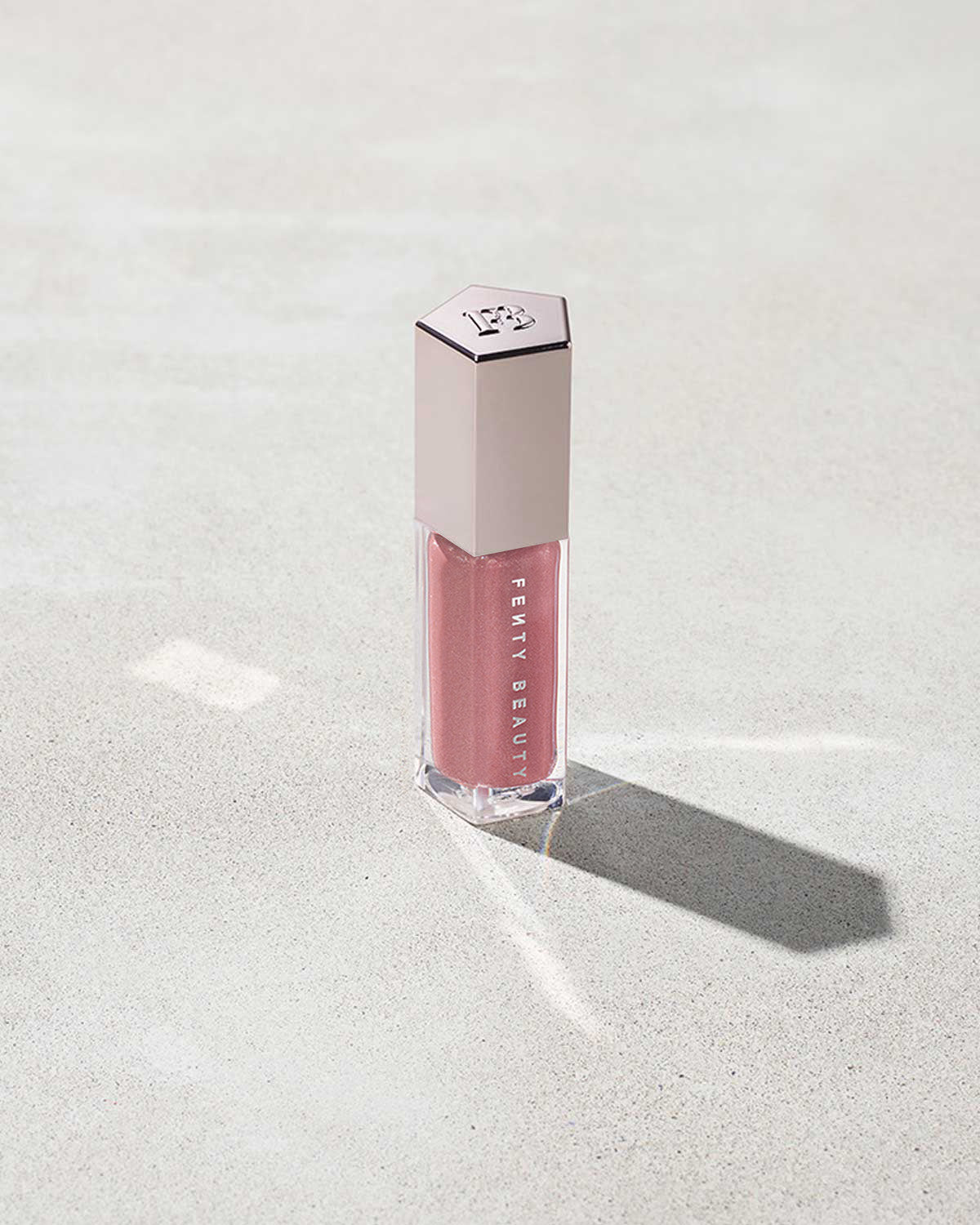 A closed tube of Gloss Bomb Universal Lip Luminizer in the shade Fu$$y on a grey background.
