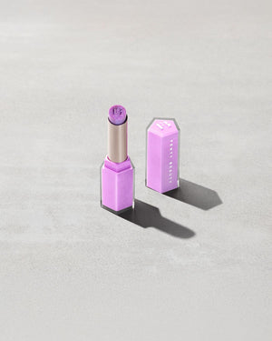 Open product shot of Gloss Bomb Stix Shimmer in shade Ice Amethyst on a concrete background.
