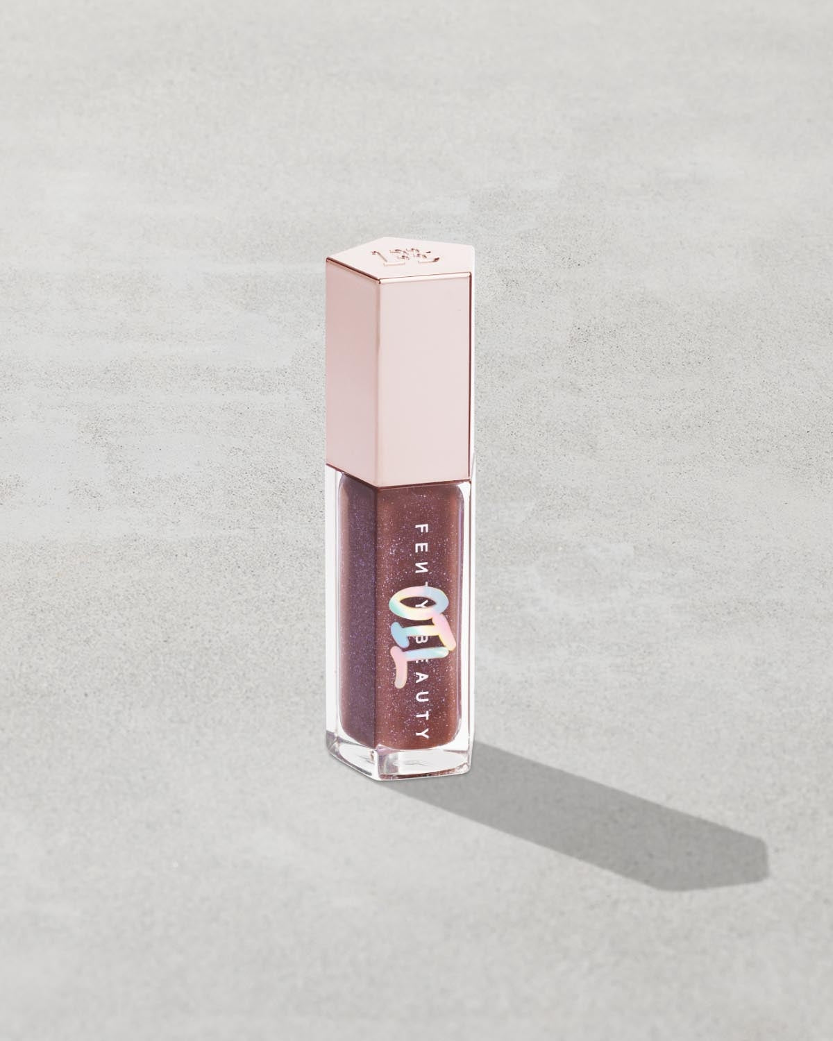 Gloss Bomb Oil Luminizing Oil and  Gloss in shade Rose Amber product against a concrete background.