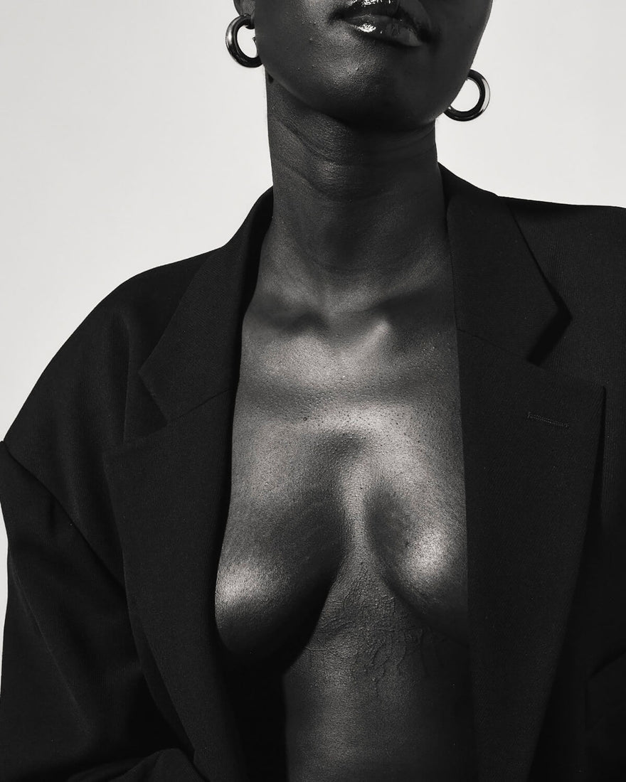 A black and white image of a woman wearing an oversized black blazer exposing their chest. 