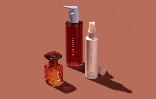 Fenty Parfum Hair + Body Mist, Fenty Skin Cherry Dub Por Purify Gel Cleanser, and You Mist Makeup-Extending Setting Spray on an orange background.