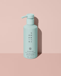 Fenty Hair The Rich One Moisture Repair Conditioner aluminum bottle with a pump on a pink background.