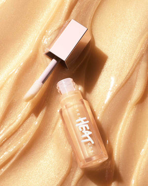 A closed tube of Gloss Bomb Heat Luminizer + Plumper with the lip gloss texture in the background.
