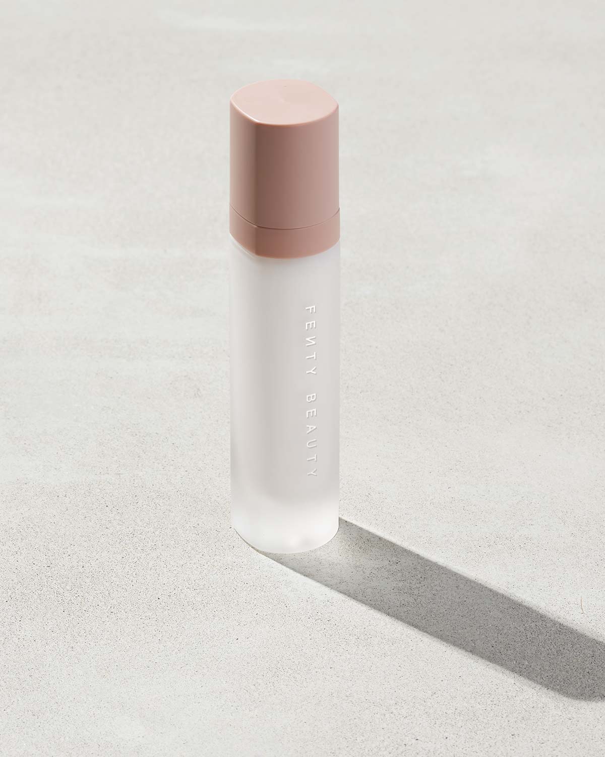 Pro Filt'r Mattifying Primer standing on a concrete-like background. The clear container showcases the primer with a pink cap.