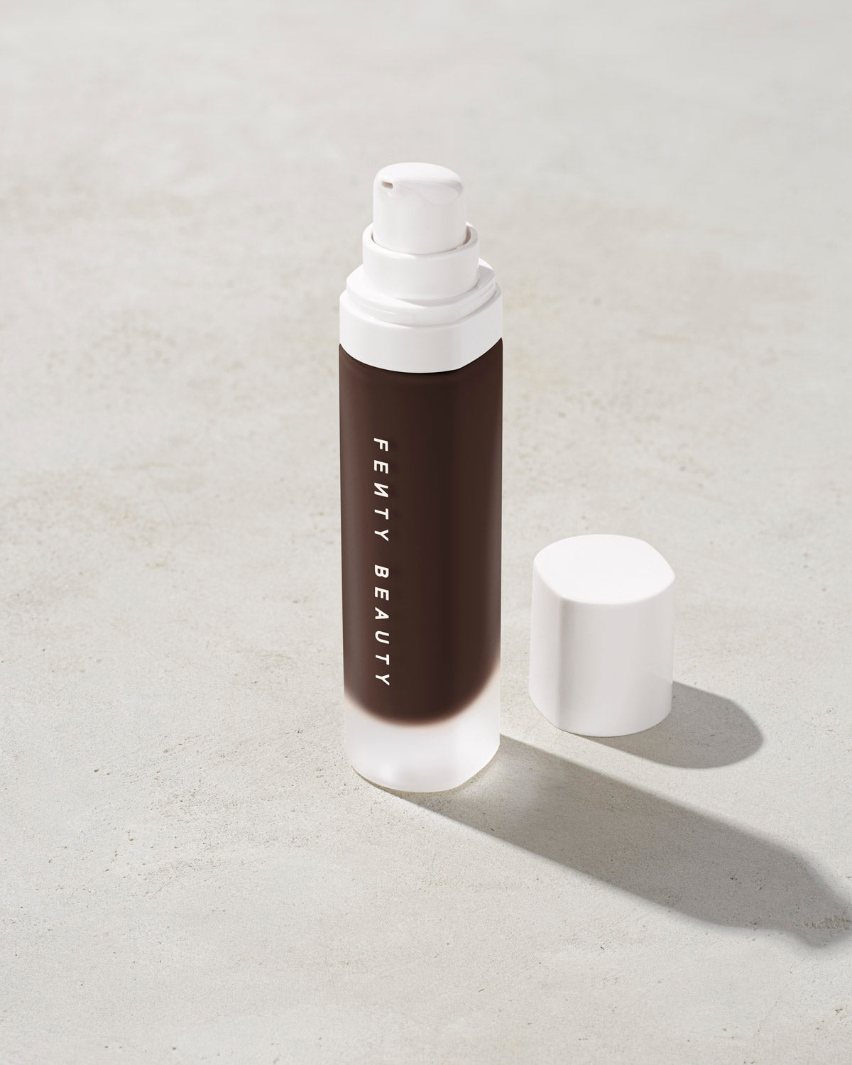open bottle of Fenty Beauty Pro Filt'r Soft Matte Longwear Foundation with pump dispenser in shade 498 on concrete background