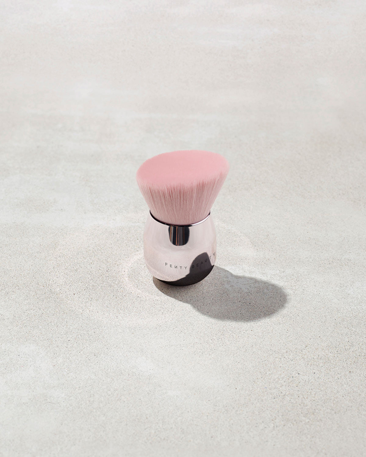 A fenty face and body kabuki brush with pink bristles on a gray background
