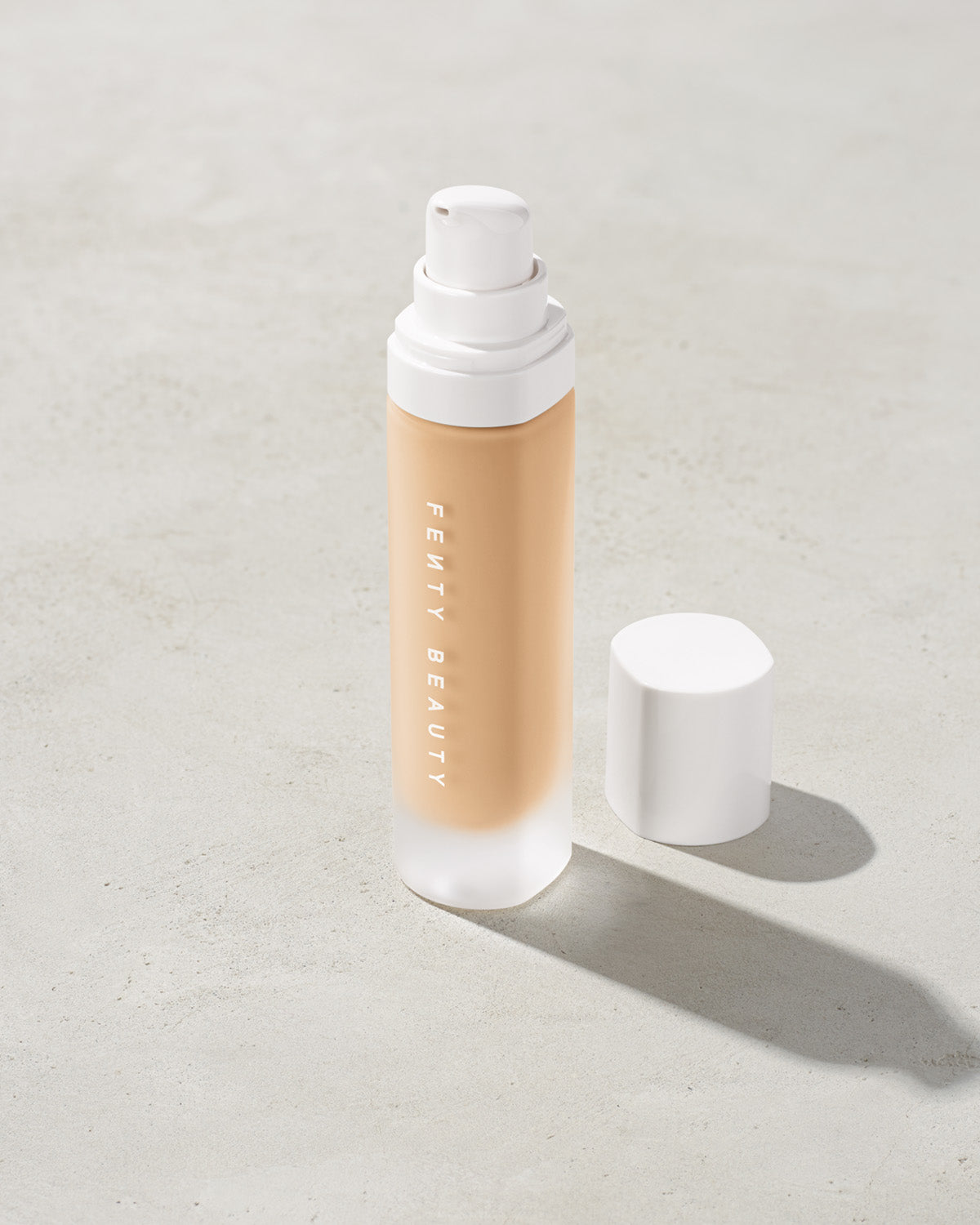 open bottle of Fenty Beauty Pro Filt'r Soft Matte Longwear Foundation with pump dispenser in shade #150 on concrete background
