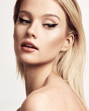 A woman of light complexion gazes to the side, showcasing the Flyliner Longwear Liquid Eyeliner, adding definition to her eyes.