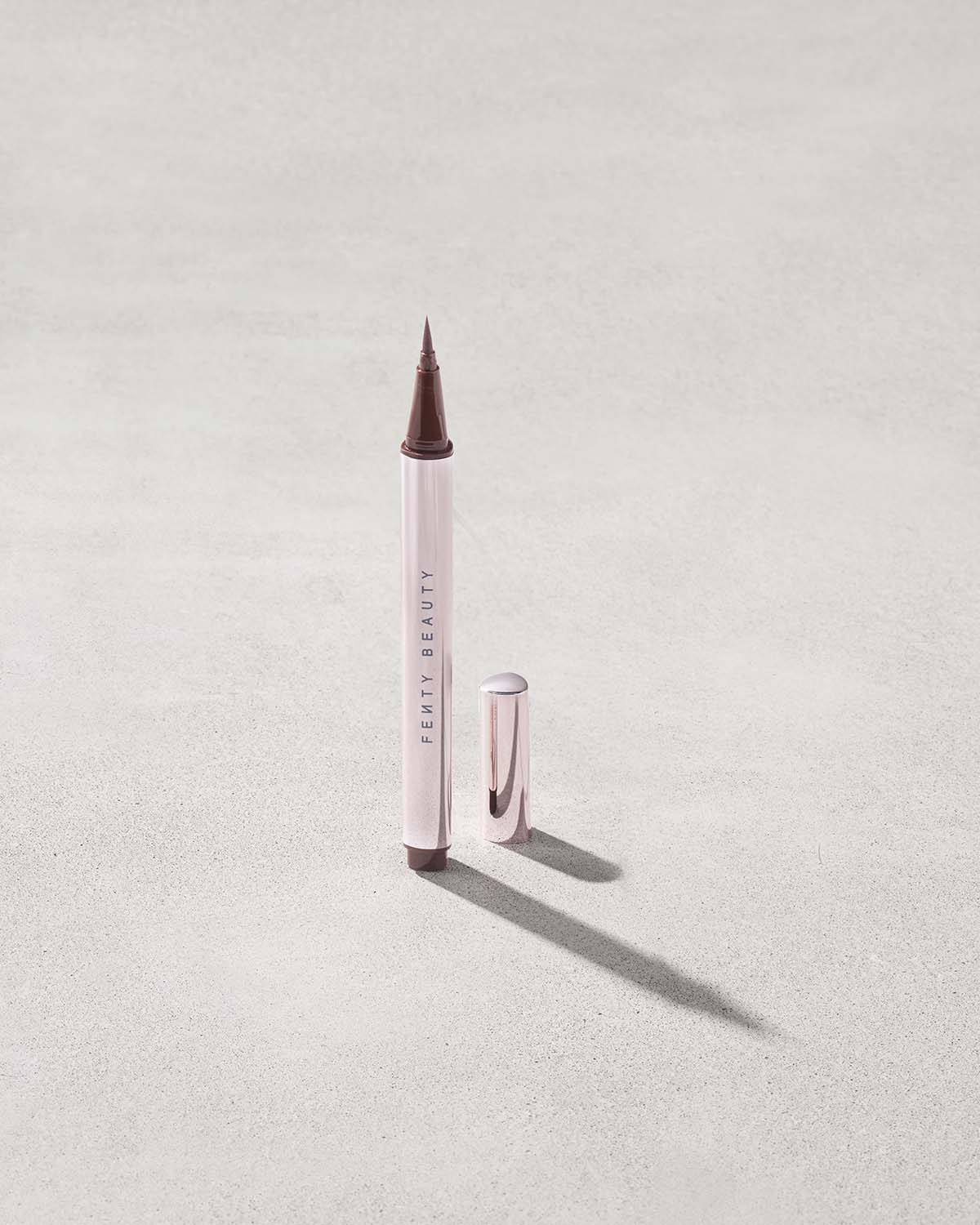 Fenty Beauty Flyliner Longwear Liquid Eyeliner in shade In Big Truffle with cap off on concrete background