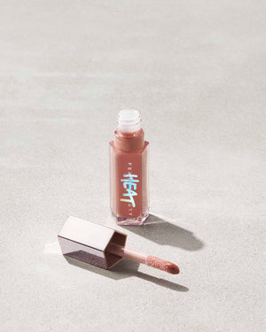 Fenty Beauty Gloss Bomb Heat Universal Lip Luminizer + Plumper in shade Fenty Glow Heat open showing doe foot applicator on concrete background